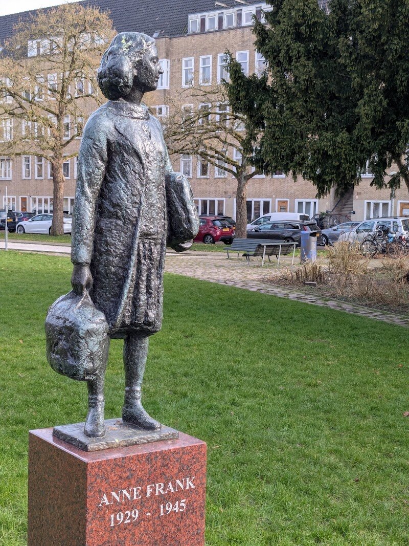 Sculpture of Anne Frank - The Sculpture of Anne Frank in Amsterdam, set in the tranquil Merwedeplein park, offers visitors a deeply moving encounter with history and hope. This evocative bronze statue depicts Anne as she was on the day her family went into hiding—layered in the many clothes she described in her diary, a poignant detail that brings her story vividly to life. Standing on a high red granite base, Anne gazes back toward her former home at 37 Merwedeplein, inviting families and curious travelers to imagine her world and the difficult choices her family faced. What makes this place special is its setting in Anne’s own childhood neighborhood, far from the crowds of the city center. Here, visitors can quietly reflect not only on Anne’s remarkable resilience but also on the fate of the thirteen thousand Jewish neighbors commemorated by the monument. Nearby, you’ll find “stumbling stones” marking the Frank family’s home, adding layers of meaning to your visit. The statue, born from a local citizens’ initiative, stands as a symbol of remembrance and a testament to the enduring impact of Anne’s life and words. For families and travelers alike, it’s a place to pause, reflect, and connect with the powerful legacy of one of history’s most beloved diarists.