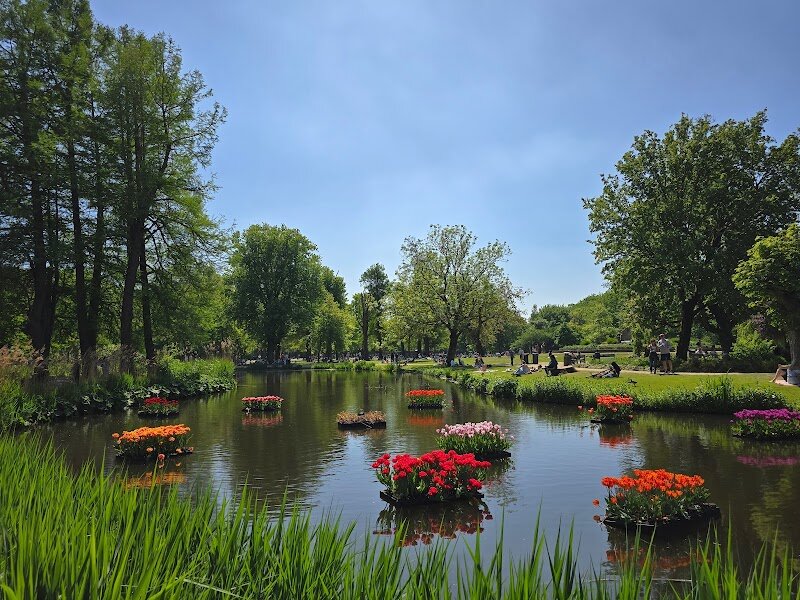 Vondelpark - Vondelpark is Amsterdam’s beloved green heart—a sprawling, 47-hectare oasis where city life melts away and every visit feels like a small adventure. Opened in 1865 and named after the famous Dutch poet Joost van den Vondel, whose statue still stands watch, the park was designed in the romantic English landscape style to create the illusion of wild, natural beauty right in the city center. Families and curious travelers will find something for everyone here: winding pathways perfect for leisurely strolls, ponds teeming with birds, and expansive lawns for picnics or play. Children can explore imaginative playgrounds, while adults might catch a free open-air theater performance or relax at the charming Blue Tea House café. Vondelpark’s history is woven into its landscape—from its beginnings as a fashionable meeting spot for horseback riders in the 19th century, to its transformation into a vibrant, inclusive space where locals and visitors alike gather for festivals, performances, and even world-record picnics. Whether you’re seeking tranquility, art, or the simple joy of a sunny afternoon, Vondelpark offers a welcoming escape at the very soul of Amsterdam.