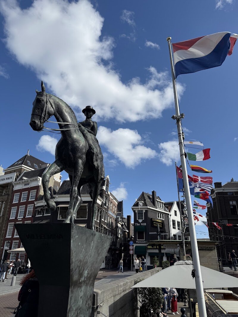 Equestrian statue of Queen Wilhelmina - The **Equestrian Statue of Queen Wilhelmina** on Rokin street is a vibrant centerpiece in Amsterdam’s historic heart, captivating families and curious travelers alike with its striking presence and rich story. Sculpted in bronze by Theresia van der Pant, this monument honors Queen Wilhelmina, who reigned for nearly 58 years and guided the Netherlands through two world wars and profound national transformation. Unlike other statues depicting her elder years, this artwork captures Wilhelmina as a young, spirited queen riding side saddle, symbolizing resilience, dignity, and leadership—a tribute shaped with input from her daughter, Queen Juliana. As you stand before the statue, you’ll be drawn into Amsterdam’s lively urban atmosphere, surrounded by bustling streets and nearby cultural gems like the UNESCO-listed Canal District and Amsterdam Museum. Children and adults alike can marvel at the detailed craftsmanship and imagine the stories of a monarch who became a beacon of hope during turbulent times. The statue’s accessible location makes it a perfect stop during a family stroll or city adventure, offering a tangible link between the city’s past and its present-day energy. Here, history comes alive, inviting everyone to reflect and explore together.