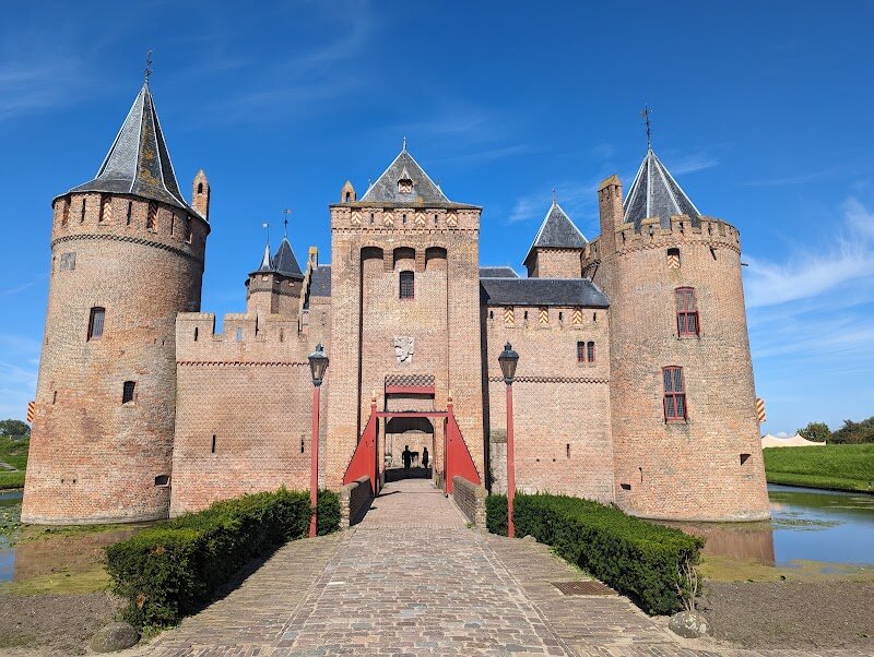 Muiderslot - Muiderslot, just a short journey from Amsterdam, is a **storybook medieval castle** that delights families and curious travelers alike with its rich history and enchanting atmosphere. Originally built in 1285 by Count Floris V to guard the vital Vecht River trade route, the castle’s dramatic past includes betrayal, destruction, and rebirth—its walls have witnessed the intrigues of knights, nobles, and poets. Rebuilt in the 14th century, Muiderslot retains its iconic square layout, round towers, and sturdy moat, inviting visitors to step into a world where legends come alive. Inside, you’ll discover **fascinating period rooms**, hands-on exhibits, and interactive experiences that bring the castle’s history to life for all ages. Families can explore the armory, wander through themed rooms, and even try on medieval costumes. The lush gardens, especially vibrant in autumn with the plum orchard harvest, offer a peaceful escape and a chance to enjoy the horticultural traditions of the estate. Muiderslot’s story also includes hosting the famous “Muiderkring,” a circle of artists and thinkers led by poet Pieter Corneliszoon Hooft, making it a hub of creativity during the Dutch Golden Age. Whether you’re seeking adventure, inspiration, or a glimpse into the past, Muiderslot promises an unforgettable experience in a truly magical setting.