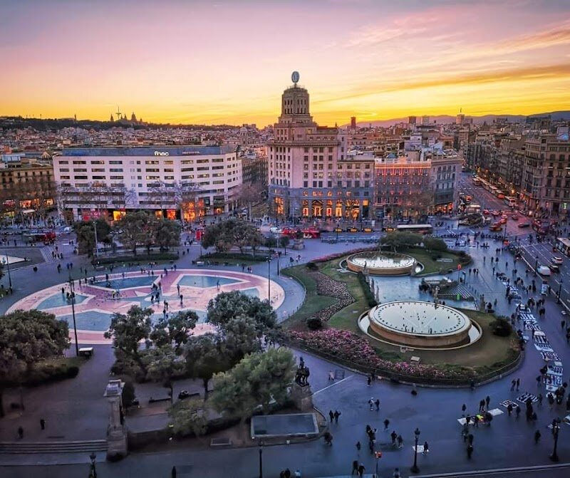 Plaça de Catalunya - Plaça de Catalunya is the vibrant heart of Barcelona, where the city’s history and present pulse together in a lively blend of energy and culture. Once a rural expanse outside the old city walls, this grand square was transformed in the early 20th century and inaugurated in 1927, becoming the symbolic link between Barcelona’s medieval core and its elegant Eixample district. Families and curious travelers will find themselves surrounded by a dynamic mix of monumental architecture, lush fountains, and striking sculptures by renowned artists such as Clarà and Llimona. It’s a perfect spot for people-watching, with locals and visitors alike gathering for everything from impromptu street performances to city-wide celebrations. Children will love chasing pigeons or exploring the square’s open spaces, while adults can appreciate the artistic details or relax on a shaded bench. Plaça de Catalunya is not just a crossroads of Barcelona’s most famous streets—La Rambla and Passeig de Gràcia—it’s a living stage for the city’s biggest moments, from historic rallies to festive parades. Whether you’re shopping, sightseeing, or simply soaking in the atmosphere, this iconic square promises a true taste of Barcelona’s spirit and vibrancy.