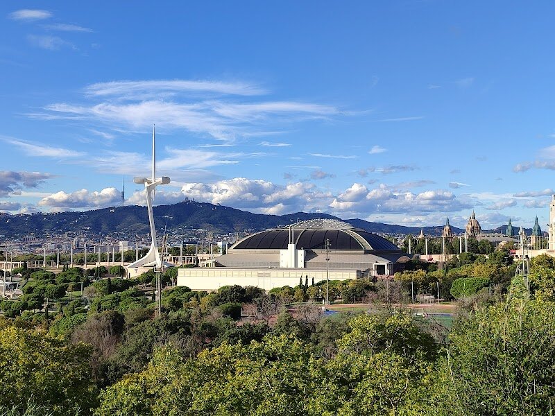 Palau Sant Jordi - Palau Sant Jordi, perched atop Barcelona’s scenic Montjuïc hill, is a marvel of modern architecture and a hub of excitement for families and explorers alike. Designed by renowned Japanese architect **Arata Isozaki** and unveiled in 1990, this striking arena became a symbol of Barcelona’s transformation during the 1992 Olympic Games, hosting pivotal events that marked the city’s leap onto the world stage. Its sweeping dome—ingeniously raised using cutting-edge hydraulic technology—evokes the organic forms of Gaudí and offers an impressive silhouette against the Barcelona skyline. Inside, visitors are welcomed into a versatile space that hosts everything from high-energy sporting competitions and international concerts to dazzling theatrical shows and family-friendly events. With a capacity to seat nearly 18,000, the arena buzzes with life and creativity, making every visit a new adventure. Beyond its walls, the surrounding Olympic Ring invites exploration, while nearby sculptures and the adjacent Sant Jordi Club add artistic flair and entertainment options for all ages. Whether you’re seeking the thrill of a live event or simply curious about Barcelona’s Olympic legacy, Palau Sant Jordi promises memories that will inspire and delight.