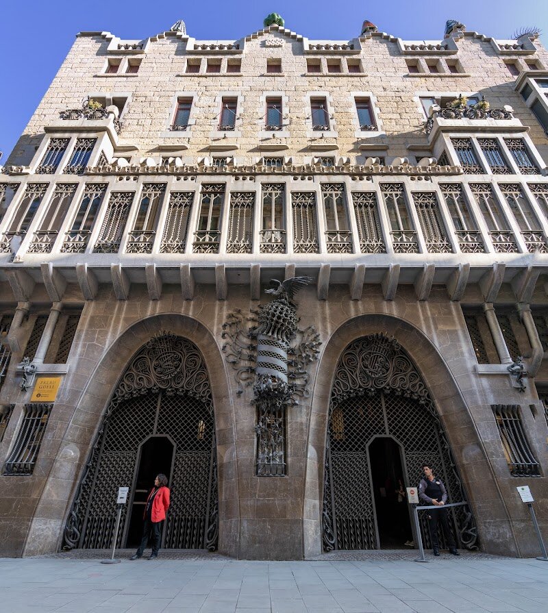 Palau Güell - Palau Güell is a dazzling architectural treasure in the heart of Barcelona, designed by the visionary Antoni Gaudí for his patron, the industrialist Eusebi Güell, between 1886 and 1888. Unlike many grand homes built in spacious districts, Güell chose the vibrant Raval neighborhood, making this urban palace a bold statement of elegance nestled among bustling city life. Families and curious travelers are captivated by the mansion’s blend of Art Nouveau and Gothic styles, its unique façade with grand catenary arches, and whimsical ironwork inspired by nature—look for sea kelp shapes and the mythical Phoenix perched atop the building. Inside, visitors discover a world of creativity: a soaring central hall crowned by a parabolic dome, vibrant stained glass windows, and a rooftop forest of twenty fantastically decorated chimneys, each a mosaic masterpiece crafted from broken ceramic tiles. Children will marvel at the play of sunlight and color, while adults appreciate the history behind every detail, from the lavish salons that once hosted royal gatherings to the stables ingeniously designed for both horses and comfort. Today, Palau Güell is not just a museum but a living monument, hosting concerts and cultural events that invite everyone to experience Gaudí’s genius and Barcelona’s rich heritage up close.