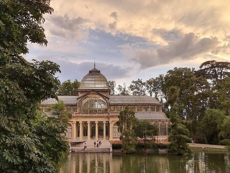 Palacio de Cristal - Nestled within the verdant expanse of Madrid's Buen Retiro Park stands the Palacio de Cristal, a breathtaking testament to 19th-century innovation and artistry. This architectural marvel, designed by Ricardo Velázquez Bosco in 1887, was originally conceived as a greenhouse to showcase exotic flora and fauna from the Philippines during a grand exhibition. What makes this structure truly enchanting is its ethereal design—a Greek cross fashioned almost entirely of glass and cast iron, crowned by a cupola soaring over 22 metres high. The intricate ironwork, manufactured in Bilbao, combines with delicate ceramic tiles by renowned Spanish ceramist Daniel Zuloaga, creating a harmonious blend of engineering prowess and artistic beauty. Today, the Palacio de Cristal belongs to the Reina Sofía Museum and serves as a dynamic venue for temporary art exhibitions. Visitors are captivated by how natural light floods through the glass panels, creating an otherworldly atmosphere that feels simultaneously protective and liberating. Surrounded by horse chestnuts and overlooking a serene pond, this glass sanctuary offers families and curious travelers an unforgettable experience where art, history, and nature converge in perfect harmony.