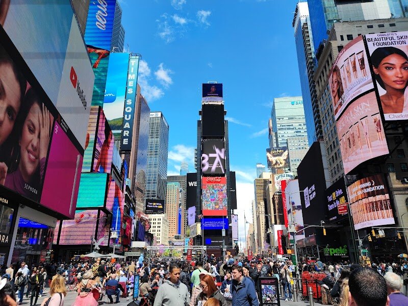 Times Square - Times Square is a dazzling tapestry of lights, energy, and excitement at the heart of New York City—a place where families and curious travelers alike feel the pulse of the metropolis. Once known as Long Acre Square, this bustling crossroads was renamed in 1904 when The New York Times moved its headquarters here, sparking a transformation from a carriage district to a world-famous entertainment hub. Strolling through Times Square, visitors are greeted by giant illuminated billboards, costumed characters, and the vibrant buzz of Broadway theaters, making it a true “Crossroads of the World”. Its history mirrors New York’s own evolution: from the glamour of early 20th-century theaters and grand hotels to a period of decline, and finally to a family-friendly revival in the 1990s that restored its welcoming spirit. Today, Times Square hosts iconic events like the annual New Year’s Eve ball drop, drawing millions of viewers worldwide. Families can enjoy street performers, interactive attractions, and the thrill of being surrounded by the city’s legendary lights. Whether you’re seeking Broadway magic, a taste of urban history, or simply the joy of people-watching, Times Square promises an unforgettable New York adventure.