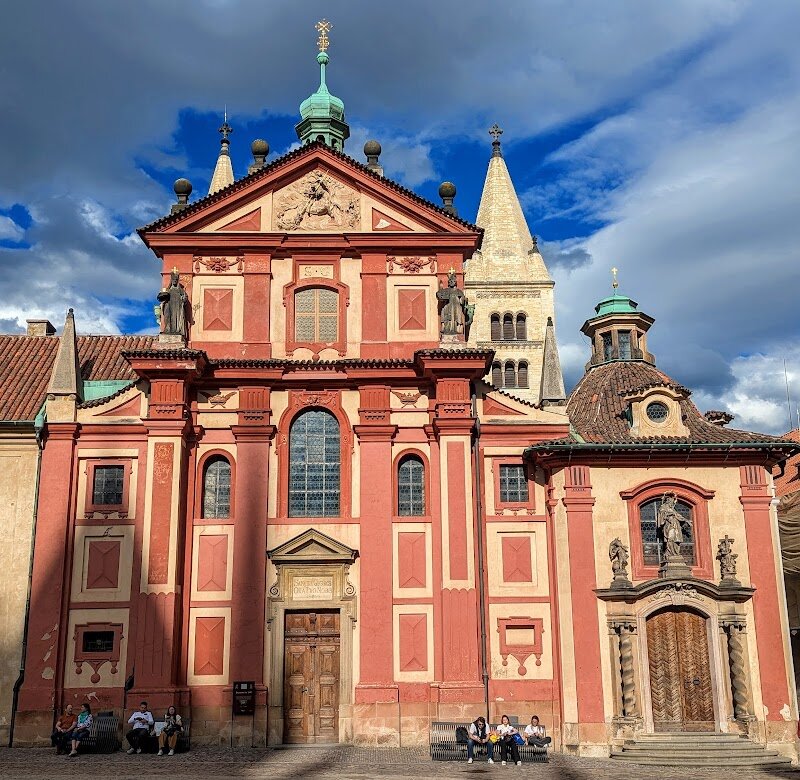 St. George's Basilica - St. George’s Basilica, nestled within the heart of Prague Castle, invites families and curious travelers to step into a living tapestry of Czech history. Founded over a thousand years ago, this awe-inspiring church is the city’s second oldest, blending **Romanesque** simplicity with a striking **Baroque façade**. Its story began in 920, when Duke Vratislav established it as a beacon for the spread of Christianity in Bohemia, later becoming the burial site of St. Ludmila, grandmother of St. Wenceslas—a legendary Czech figure. Inside, visitors will discover a serene, **three-nave interior** with wide arches, ethereal light streaming through ancient windows, and a haunting crypt that whispers tales of centuries past. Children and adults alike will be fascinated by the basilica’s two towers, affectionately named “Eve” and “Adam,” each with its own history and character. Art and architecture enthusiasts will appreciate the blend of Romanesque and Baroque styles, while history lovers can explore the story of the Benedictine convent and the royal dynasties connected to the basilica. Whether you’re seeking a quiet moment or a hands-on lesson in Prague’s spiritual and royal heritage, St. George’s Basilica offers a captivating experience for all ages.