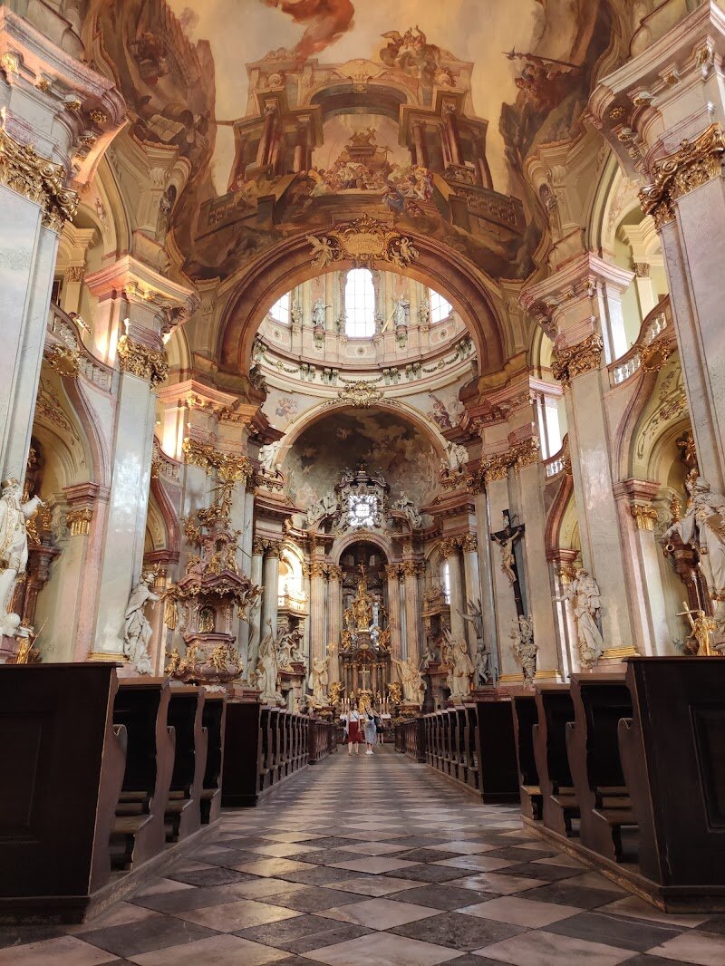 St. Nicholas Church (Malá Strana) - St. Nicholas Church in Prague’s Malá Strana is a dazzling Baroque masterpiece that enchants visitors of all ages with its soaring dome, ornate interiors, and rich history stretching back to the 13th century. Rising just steps from the Charles Bridge, this church captivates families and curious travelers with its dramatic architecture—look up to marvel at one of Europe’s largest ceiling frescoes, the breathtaking “Apotheosis of St. Nicholas,” painted in 1761 by Johann Kracker. Built between 1704 and 1755 on the site of an older Gothic church, St. Nicholas Church was shaped by some of the greatest Baroque architects, including Christoph and Kilian Ignaz Dientzenhofer, whose vision brought to life the church’s grand nave and striking copper cupola. Inside, you’ll discover a world of exquisite marble, gilded carvings, and monumental statues. For music lovers, the church’s mighty organ—once played by Mozart himself—still fills the space during regular concerts, making every visit a multisensory delight. Families can climb the 80-meter bell tower for stunning views over Prague’s rooftops, while history buffs will appreciate the church’s role through centuries of religious change, royal patronage, and even Cold War intrigue. Whether you’re drawn by art, music, or stories, St. Nicholas Church offers a feast for the imagination in the heart of Prague.