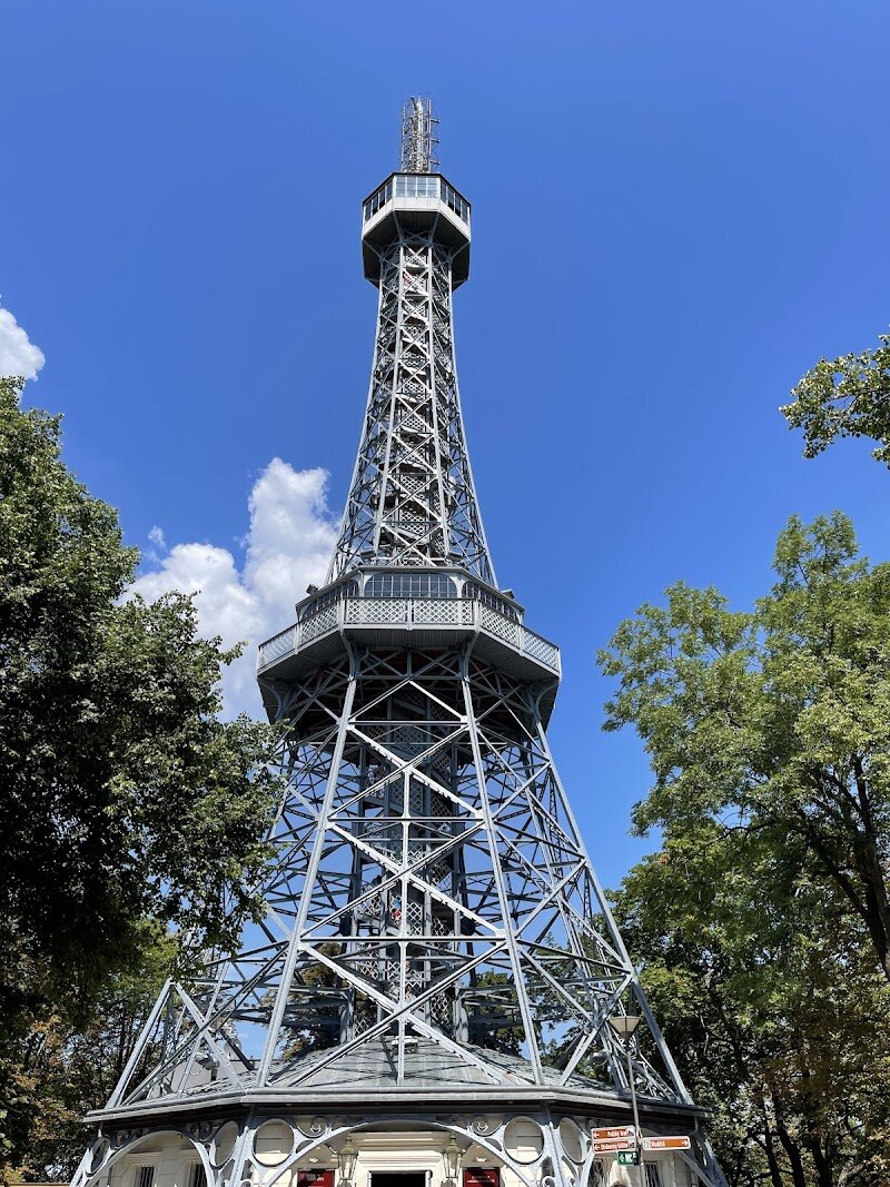Petrin Tower - Rising gracefully above Prague’s lush Petřín Hill, **Petřín Tower** is a beloved icon for families and curious travelers alike. Built in 1891 for the Jubilee Exhibition, this steel marvel was inspired by the Eiffel Tower after Czech visionaries visited Paris and dreamed of bringing a similar landmark to their city. While only one-fifth the size of its Parisian cousin, Petřín Tower’s summit matches the Eiffel’s altitude, thanks to its hilltop perch—offering breathtaking, panoramic views over Prague’s spires, bridges, and gardens. Climbing the 299 steps (or riding the elevator) to the observation decks is an adventure for all ages, rewarded by vistas stretching across the city and, on clear days, into distant Bohemia. The journey begins with a scenic stroll or funicular ride through Petřín’s tranquil park, making it a perfect outing for families wanting to blend nature and history. Beyond its architectural charm, Petřín Tower has endured dramatic chapters—including wartime threats and decades as a TV transmitter—before being lovingly restored for new generations to enjoy. Today, its playful silhouette and interactive climb make it an unforgettable highlight of any Prague adventure.