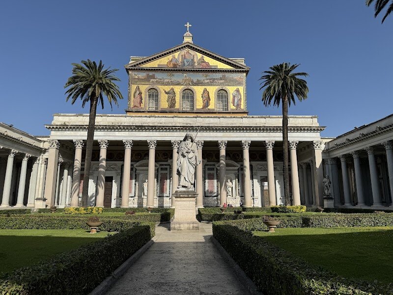 Basilica of Saint Paul Outside The Walls - The Basilica of Saint Paul Outside the Walls is an awe-inspiring treasure in Rome, inviting families and curious travelers to step into centuries of history and artistry. As the second largest of Rome’s four papal basilicas, it stands on the site where, according to tradition, the Apostle Paul was buried, making it not only a place of worship but also a powerful link to the roots of Christianity. The basilica’s origins date back to Emperor Constantine in the 4th century, with later expansions reflecting the growing number of pilgrims who came to honor Saint Paul. Visitors are greeted by a grand quadriportico lined with 150 columns, leading to a façade adorned with shimmering mosaics and the impressive statue of Saint Paul. Inside, families can marvel at the vast nave, intricate chapels, and the golden apse mosaic, all restored after a devastating fire in the 19th century. One highlight is the series of medallions depicting every pope in history—a visual timeline that sparks curiosity in kids and adults alike. Whether you’re exploring the peaceful cloister, admiring ancient relics, or simply soaking in the serene atmosphere, Saint Paul Outside the Walls offers a unique blend of spiritual heritage and artistic wonder, making it a memorable stop for every traveler in Rome.