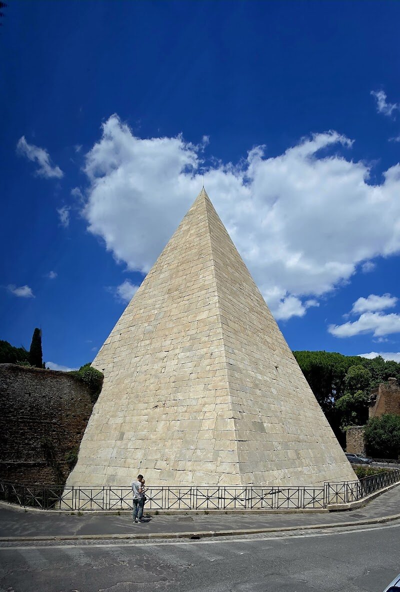 Pyramid of Caius Cestius - ## The Pyramid of Caius Cestius: Rome’s Egyptian Marvel Imagine wandering through the heart of Rome and suddenly spotting a gleaming white pyramid—an unexpected sight that whisks you from the cobblestones of Italy to the sands of Egypt. The Pyramid of Caius Cestius, built between 18 and 12 BC, is one of the city’s most intriguing monuments, a striking testament to ancient Rome’s fascination with all things Egyptian. Commissioned as a tomb for Gaius Cestius, a wealthy magistrate and priest, this pyramid was his final, flamboyant statement—so determined was he to be buried in Egyptian style that he ordered its completion within just 330 days of his death, or his heirs would lose their inheritance. What makes this pyramid truly special is its survival. Unlike Rome’s other ancient pyramids, long since lost to history, Cestius’ tomb was ingeniously incorporated into the Aurelian Walls in the 3rd century, ensuring its preservation through the ages. Today, it stands proudly near the bustling Piramide metro station, a silent guardian of stories from two millennia past. Families and curious travelers will be captivated by the pyramid’s crisp, steep angles—inspired not by the pyramids of Giza, but by those of Nubia, reflecting the eclectic tastes of Rome’s elite. The marble-clad exterior still bears inscriptions detailing Cestius’ life and his unusual final wish, offering a tangible connection to the person behind the monument. Although the burial chamber is rarely open to the public, its vividly painted walls—adorned with nymphs, winged Victories, and lost treasures—hint at the opulence within. A visit here is more than a photo opportunity; it’s a journey through layers of history, myth, and cultural exchange. For children, it’s a real-life treasure hunt, and for adults, a poignant reminder of how the ancient world was far more interconnected than we often imagine. The Pyramid of Caius Cestius isn’t just a relic—it’s a bridge between civilizations, waiting to spark your curiosity in the Eternal City.