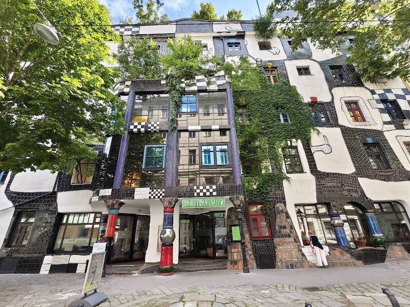 Kunst Haus Wien. Museum Hundertwasser - Nestled in Vienna's charming Weißgerberviertel, Kunst Haus Wien stands as a vibrant testament to artistic vision and ecological consciousness. Opened in 1991, this architectural marvel was transformed by the visionary Friedensreich Hundertwasser from a 19th-century furniture factory into something truly extraordinary. The moment you step inside, you enter a world where straight lines seem to vanish. Undulating floors, curved walls adorned in bold colors, and shimmering mosaics create an immersive experience that challenges conventional design. Hundertwasser's philosophy comes alive through every detail—from the lush vertical gardens and tree-integrated façades to the innovative "humus toilettes" and plant-based water treatment systems. The museum houses the world's most comprehensive collection of Hundertwasser's work, spanning paintings, tapestries, and architectural models across two exhibition floors. Beyond his artistic creations, you'll discover how this restless painter, architect, and environmentalist reimagined what a museum could be—a living, breathing space where nature and art intertwine. Whether you're an art enthusiast or simply curious about unconventional design, this green museum offers a refreshingly different perspective on creativity and sustainability.