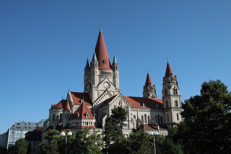 St. Francis of Assisi Church - Nestled beside the Danube River in Vienna's 2nd district, St. Francis of Assisi Church stands as one of the city's most enchanting architectural treasures. Built between 1898 and 1910, this magnificent basilica was constructed to celebrate the 50th anniversary of Emperor Franz Joseph I's reign and consecrated in 1913. Designed by renowned architect Victor Luntz, the church captivates visitors with its striking Rhenish-Romanesque style, featuring three distinctive red-tiled towers that are visible from kilometers away. What truly sets this church apart is its emotional depth. The Art Nouveau Elisabethkapelle (Elizabeth Chapel) serves as a poignant memorial to Empress Elisabeth, decorated with shimmering gold mosaics and marble walls. The chapel's octagonal design mirrors the famous Palatine Chapel in Aachen Cathedral, creating an intimate space of remarkable beauty. From the pedestrian Reichsbrücke bridge, the church resembles a fairytale castle rising majestically against the Vienna skyline. Whether you're an architecture enthusiast, history lover, or simply seeking spiritual tranquility, this lesser-known gem offers a uniquely moving experience that captures the grandeur and romance of imperial Vienna.