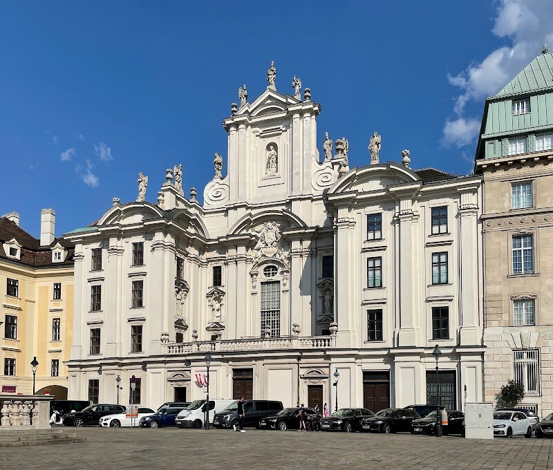 Kirche am Hof - Kirche am Hof stands as Vienna's most captivating architectural paradox—a Gothic masterpiece disguised in Baroque splendor. Located on the largest square in Vienna's inner city, this church has witnessed over six centuries of Austrian history unfold around it. Built between 1386 and 1403 by the Carmelite order on the site of a former ducal palace, the church's interior reveals its medieval Gothic roots: a soaring three-aisled hall with elegant ribbed vaults. Yet the moment you step outside, a stunning white Baroque façade greets you—a dramatic transformation completed in 1662 that dominates the entire plaza. What makes Kirche am Hof truly special is its role in pivotal historical moments. In 1806, the end of the Holy Roman Empire was declared from this church's balcony after Napoleon's occupation. The building has survived fires, religious upheaval, and centuries of change, each era leaving its mark on the structure. Today, visitors can admire the intricate Rococo organ from 1763 and explore how Baroque restoration work seamlessly blended with medieval architecture. Whether you're drawn to history, architecture, or simply seeking a moment of tranquility in Vienna's bustling city center, Kirche am Hof offers an unforgettable glimpse into the city's layered past.